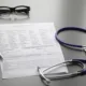 Questionnaire médical, lunettes, stylo et stéthoscope posés sur une table, pour l'assurance de prêt