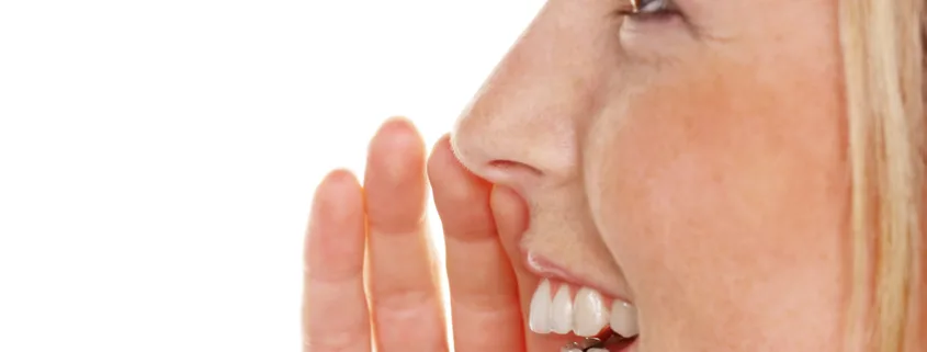Jeune femme en gros plan, une main près de la bouche comme pour confier un secret