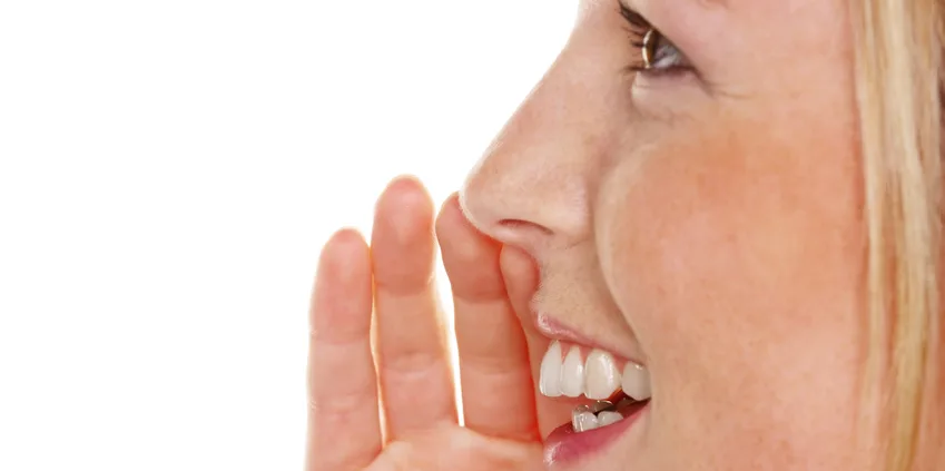 Jeune femme en gros plan, une main près de la bouche comme pour confier un secret