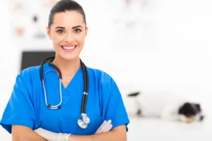 pretty veterinarian Vétérinaire souriante en blouse bleue, stéthoscope autour du cou, chien en arrière-plan
