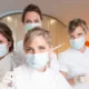 Quatre assistantes dentaires masquées en blouse blanche posant dans un cabinet