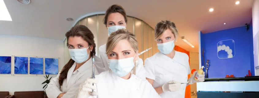 Quatre assistantes dentaires masquées en blouse blanche posant dans un cabinet