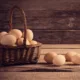 Panier en osier rempli d'œufs, d'autres œufs posés sur une table en bois