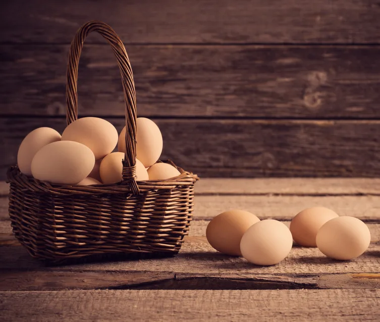 Panier en osier rempli d'œufs, d'autres œufs posés sur une table en bois