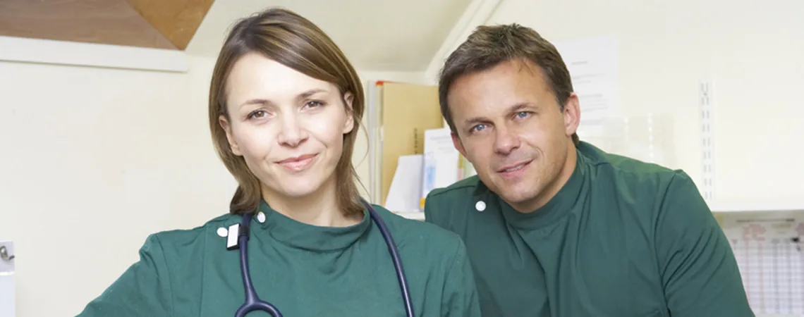 Un vétérinaire et sa conjointe en blouse verte, stéthoscope autour du cou, dans la clinique