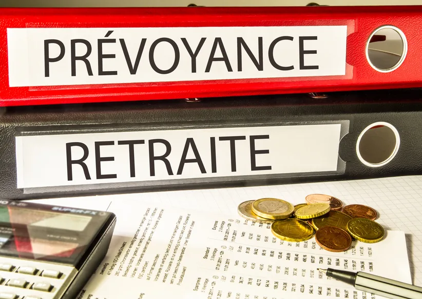 Classeurs « Prévoyance » et « Retraite » posés sur des relevés chiffrés, pièces et calculatrice